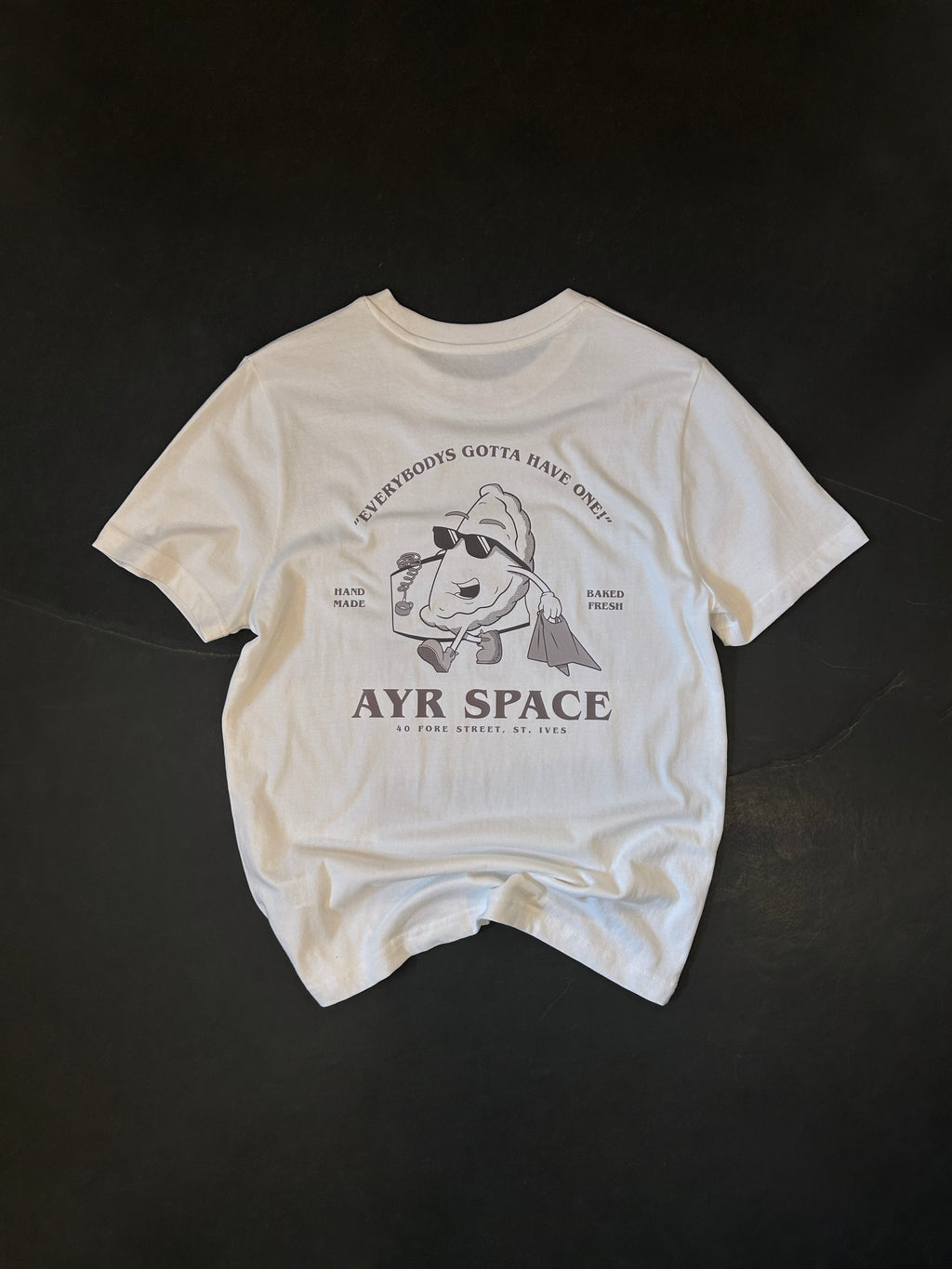 Back of the AYR SPACE Pasty T in off-white, laid flat: retro cartoon pasty in sunglasses carrying a paper bag, printed in faded brown under "Everybody's gotta have one!"