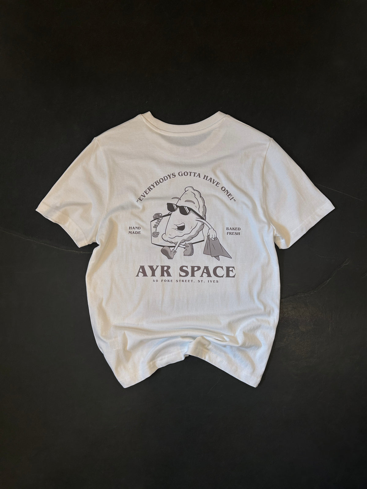 Back of the AYR SPACE Pasty T in off-white, laid flat: retro cartoon pasty in sunglasses carrying a paper bag, printed in faded brown under "Everybody's gotta have one!"