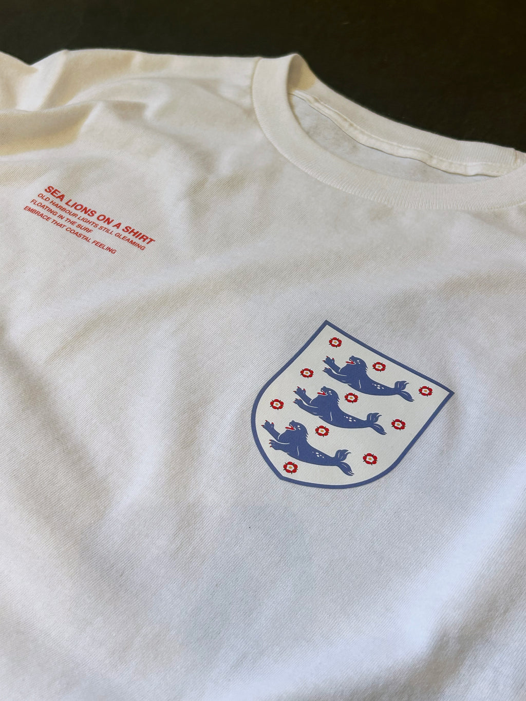 Close-up of the Sea Lions Long Sleeve in Home White: retro-style crest with three sea lions on the chest, beside the red "Sea Lions on a Shirt" text print