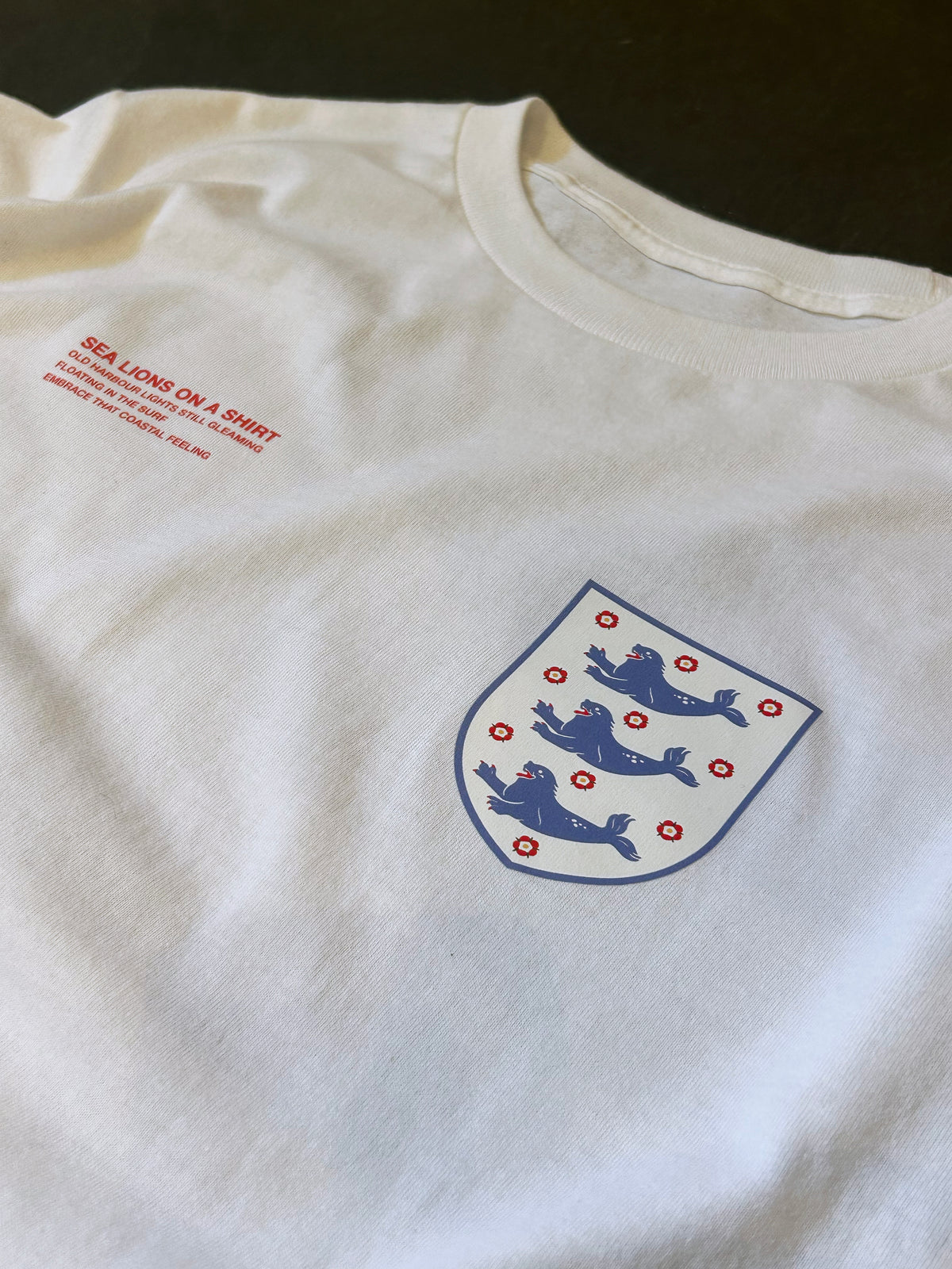 Close-up of the Sea Lions Long Sleeve in Home White: retro-style crest with three sea lions on the chest, beside the red "Sea Lions on a Shirt" text print