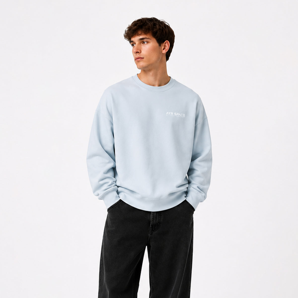 Young man wearing light blue crewneck oversized sweatshirt with 'AYR SPACE' printed in white on the left chest, with small 'st. ives - cornwall' detail underneath. displayed flat against a solid white background.